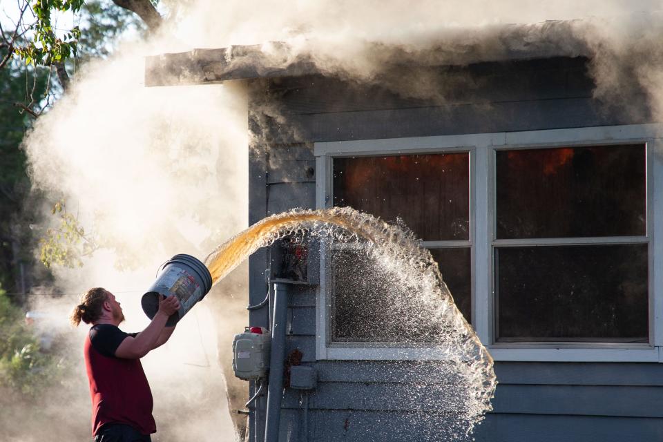 Billie Mincks tosses a bucket of Suwannee River water onto a neighboring home that caught fire in Suwannee, Fla., just a day after Hurricane Idalia made its way through Florida.