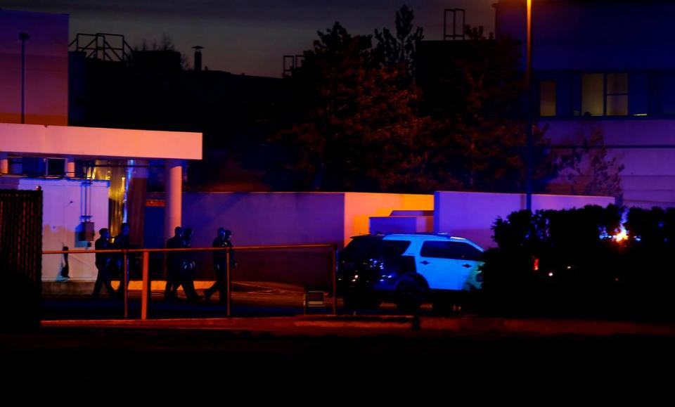 A group of Kennewick Police officers walk behind the former Kennewick General hospital building illuminated in the early morning darkness by flashing patrol car emergency lights on January 25, 2023 in downtown Kennewick.