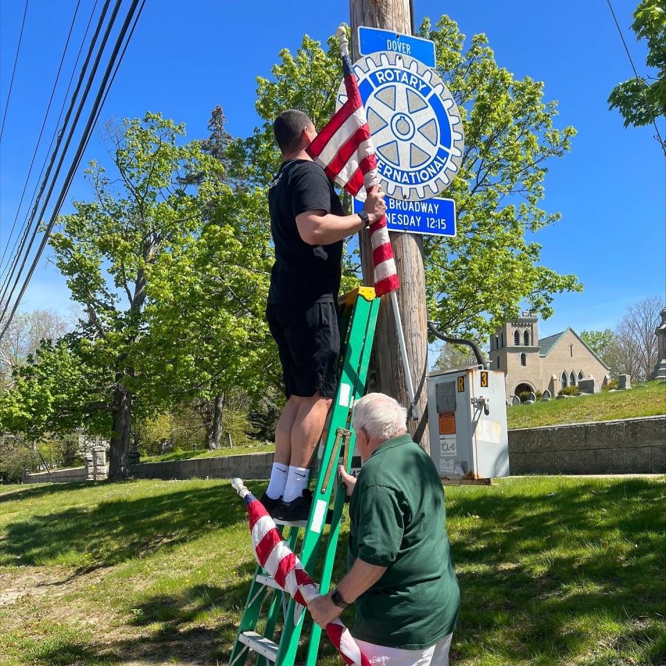 Bill Stowell of Central Park Garage (above) hangs an American flag in front of Pine Hill Cemetery on May 13 with the help of Phil Rinaldi of the Dover Rotary Club.