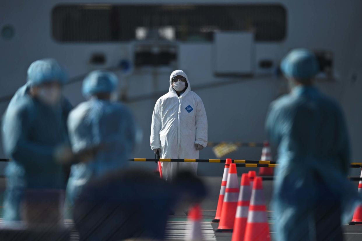 Workers in protective clothes stand before passengers disembarkating off the Diamond Princess: AFP via Getty Images