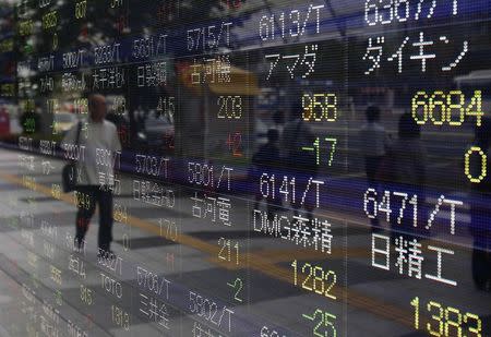 A pedestrian is reflected in an electronic board showing the various stock prices outside a brokerage in Tokyo August 13, 2014. REUTERS/Yuya Shino