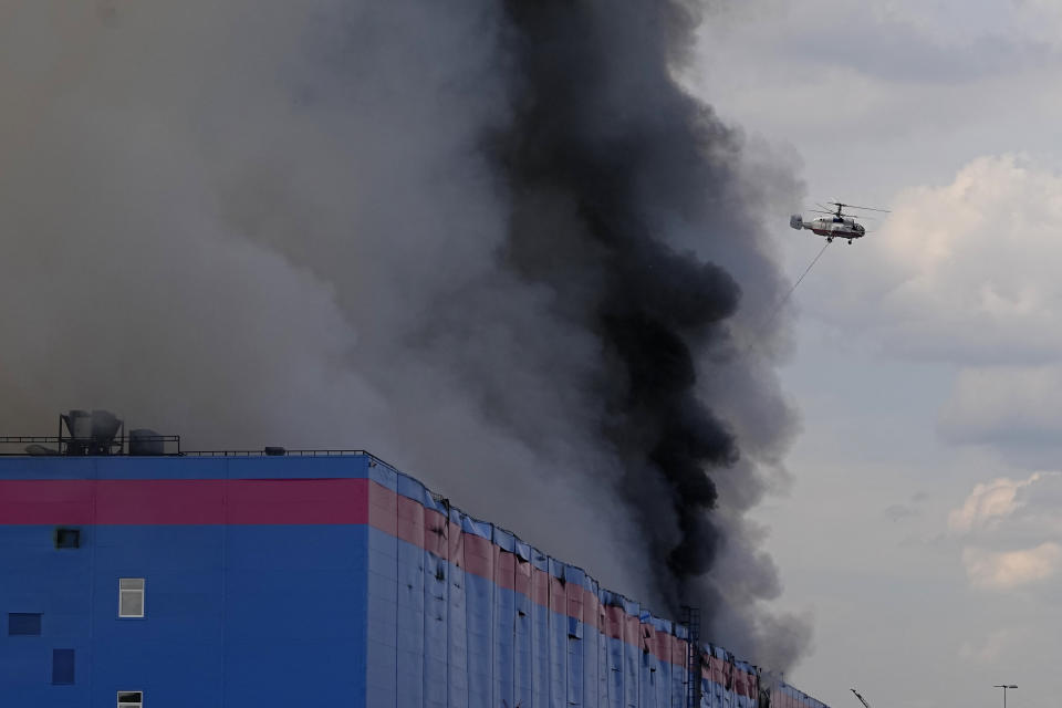 A helicopter extinguishes fire at a warehouse of the online retailer Ozon in Istra Municipal District, northwest Moscow Region, Russia, Wednesday, Aug. 3, 2022. The fire, which erupted at the warehouse belonging to Russia's leading online retailer Ozon, has covered the area of 50,000 square meters and injured 11 people, two of whom were hospitalized. (AP Photo/Alexander Zemlianichenko)