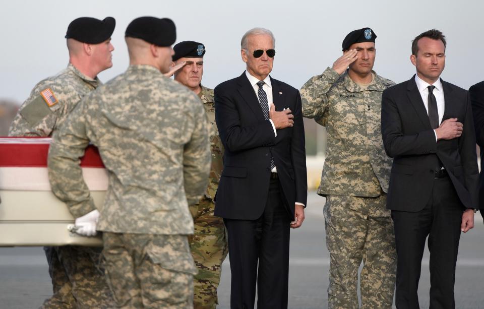 Biden with right hand on heart and soldiers saluting as coffin is carried