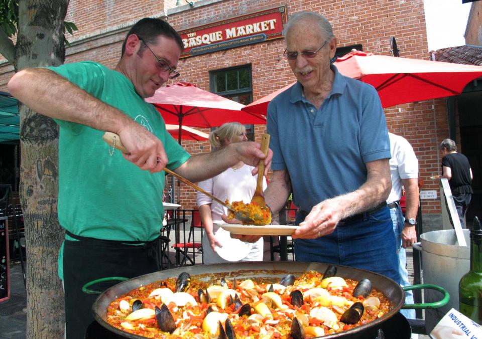 This Aug. 7, 2013 photo shows Tony Eiguren, left, owner of the Basque Market, serving a plate of paella to a lunch customer in Boise, Idaho. Each Wednesday and Friday, Eiguren and his staff make a big batch of paella in front of their store on Boise's historic Basque Block. The city’s Basque Block downtown is the best place for learning more about the heritage. As early the late 1800s, Basques began settling in southwestern Idaho, many lured here to work as sheepherders. The Basque Block includes a museum, a market, restaurants, street art and historical signage. (AP Photo/Todd Dvorak)