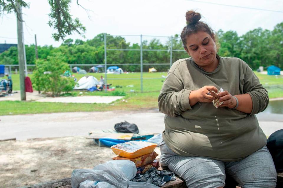 Ashley Pierce, who has been experiencing homelessness for 3 months, eats a snack while sitting at an encampment at the former Mercy Cross High School in Biloxi on Tuesday, May 14, 2024. Mercy Cross Center will soon open on the property to assist Pierce and other unhoused people in finding permanent homes.