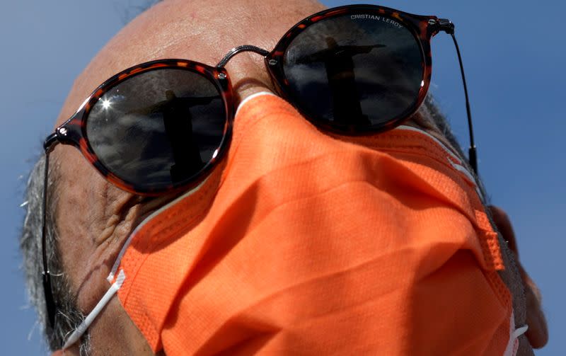 FILE PHOTO: The statue of Christ the Redeemer is reflected on the sunglasses of a tourist wearing a protective face mask during a visit after reports of coronavirus in Rio de Janeiro