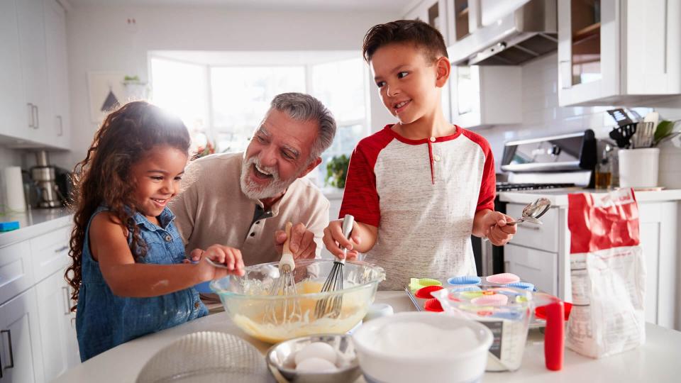 Brother and sister standing at the kitchen table making cake mix with their grandfather, close up.