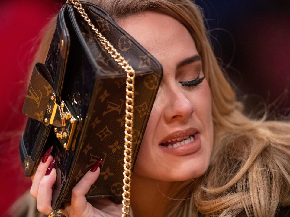 Adele looking down and covering half her face with her Louis Vuitton purse.