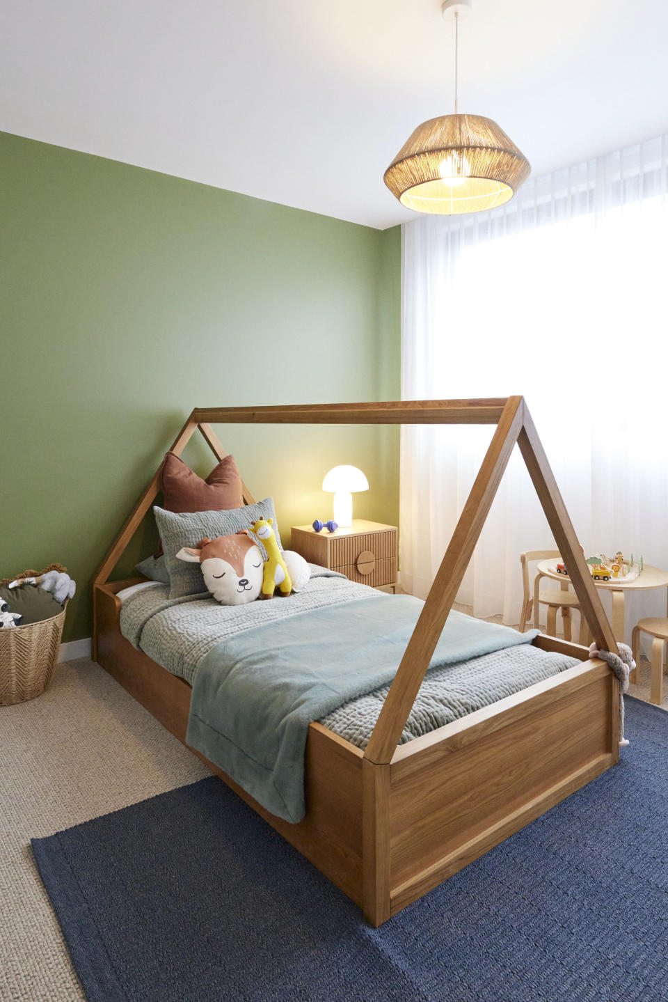 A shot of a single bed with a posters in a triangular shape above it, in front of a green wall and on a blue rug. 