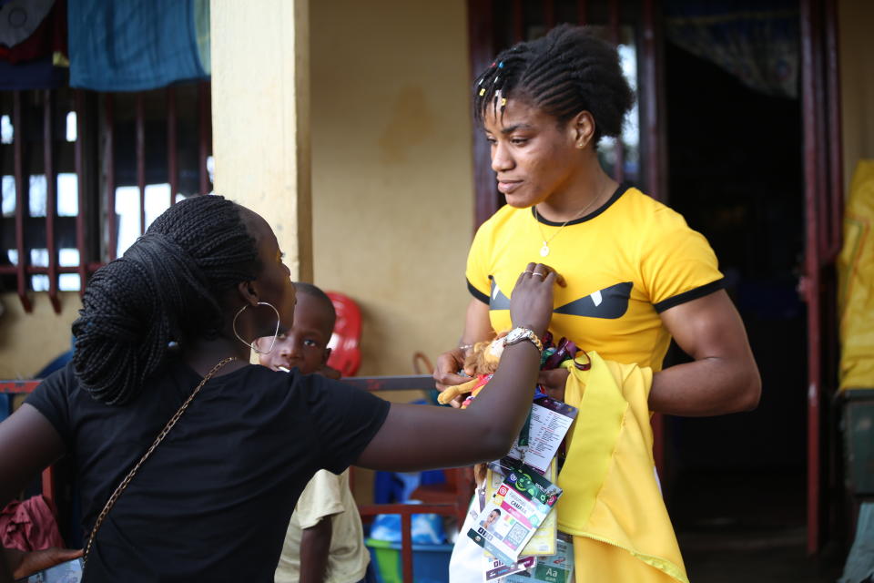 Guinean wrestler Fatoumata Yarie Camara, right, holding past credentials and medals, is greeted at her house in Conakry, Guinea, Monday July 19, 2021. A West African wrestler's dream of competing in the Olympics has come down to a plane ticket. Fatoumata Yarie Camara is the only Guinean athlete to qualify for these Games. She was ready for Tokyo, but confusion over travel reigned for weeks. The 25-year-old and her family can't afford it. Guinean officials promised a ticket, but at the last minute announced a withdrawal from the Olympics over COVID-19 concerns. Under international pressure, Guinea reversed its decision. (AP Photo/Youssouf Bah)