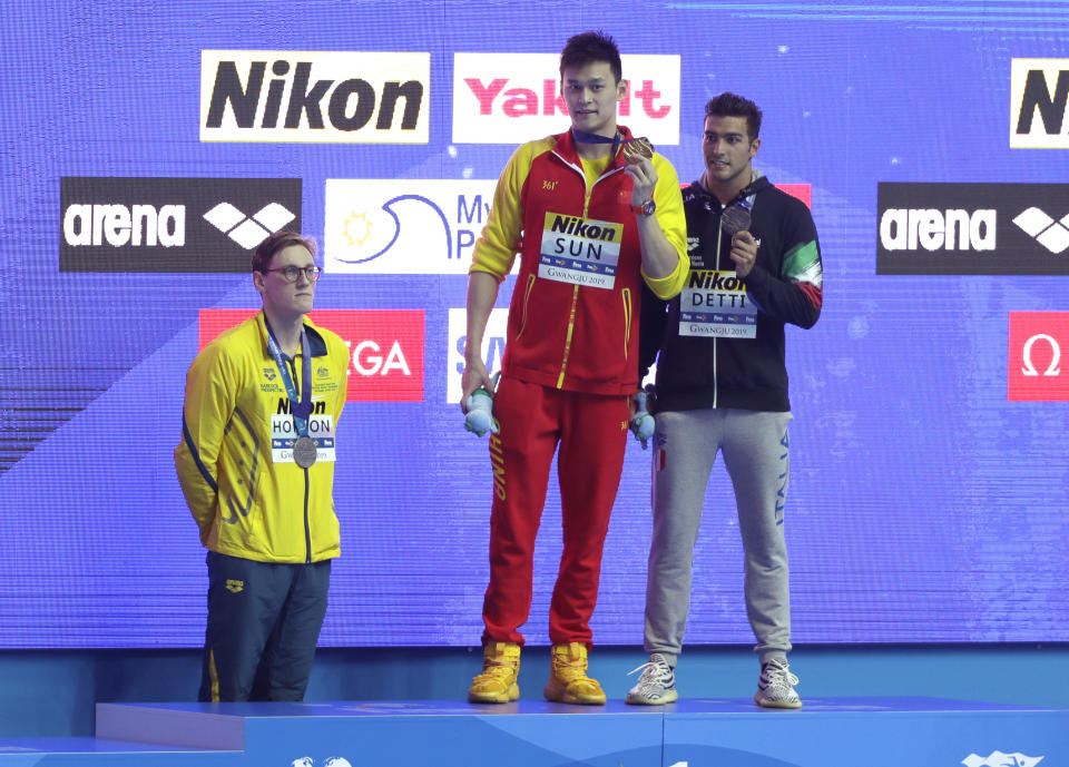FILE - In this Sunday, July 21, 2019 file photo, China's Sun Yang, centre, holds up his gold medal as silver medalist Australia's Mack Horton, left, stands away from the podium with bronze medalist Italy's Gabriele Detti at right, after the men's 400m freestyle final at the World Swimming Championships in Gwangju, South Korea. One of China’s biggest Olympic stars will undergo a rare public trial of a doping case on Friday, Nov. 15, 2019 with his 2020 Tokyo Games place at stake. Three-time gold medalist swimmer Sun Yang is facing a World Anti-Doping Agency appeal in Switzerland that seeks to ban him for up eight years. (AP Photo/Mark Schiefelbein, File)