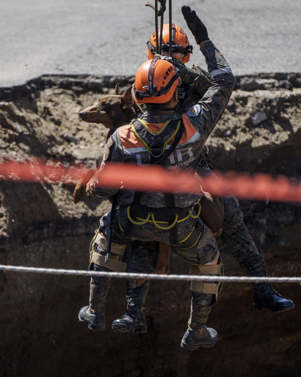 Rescuers of the Guatemalan Army and a search dog descend into a sinkhole in Villa Nueva, Guatemala, Sunday, Sept. 25, 2022. Rescuers are searching for people who are believed to have fallen into the sinkhole while driving their vehicle, while four others were rescued alive from the scene on Saturday night. (AP Photo/Moises Castillo)