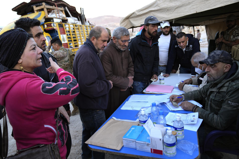 Syrian refugees checks their names with Lebanese General Security officers, right, at a gathering point where they prepare to cross the border back home to Syria, in the eastern Lebanese border town of Arsal, Lebanon, Wednesday, Oct. 26, 2022. Several hundred Syrian refugees boarded a convoy of trucks laden with mattresses, water and fuel tanks, bicycles – and, in one case, a goat – Wednesday morning in the remote Lebanese mountain town of Arsal in preparation to return back across the nearby border.(AP Photo/Hussein Malla)