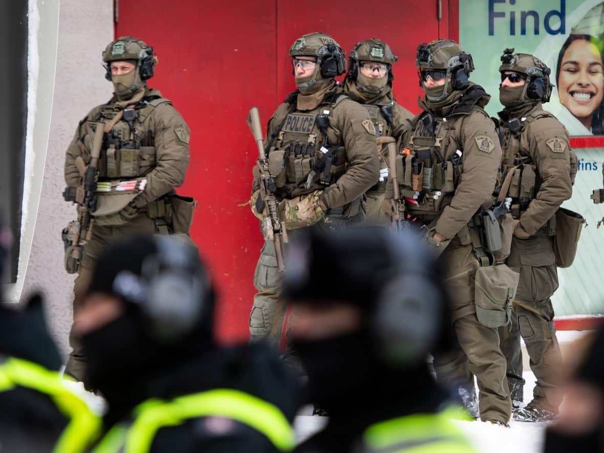 RCMP tactical officers stand behind uniformed officers as they prepare to clear protesters from a blockade of vehicles on Rideau Street on Friday, Feb. 18, 2022. (The Canadian Press - image credit)