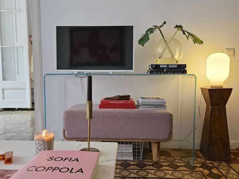 A TV on a glass stand with plants and coffee table books.