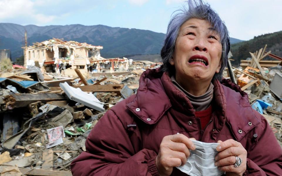 An elderly woman cries in front of a destroyed building in the devastated town of Rikuzentakata in Iwate prefecture eight days after the disaster in March 2011. Many local residents are still struggling to rebuild their lives. - NICHOLAS KAMM /AFP
