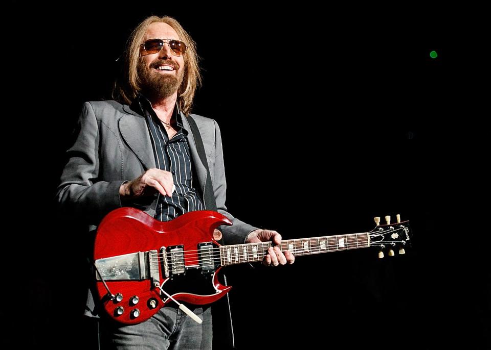 tom petty smiles while holding a electric guitar