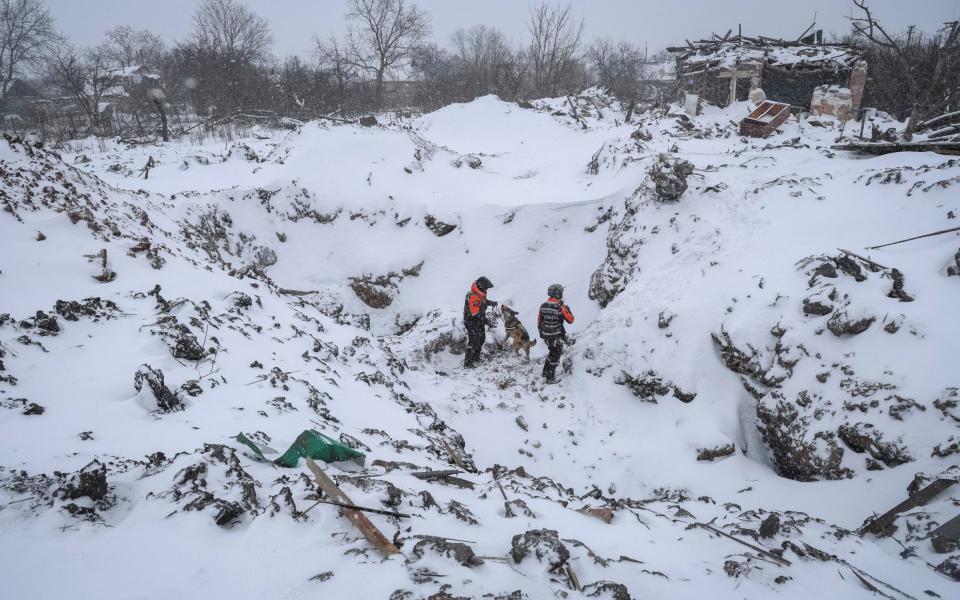 A rescue dog works with two handlers at the snow-covered site of a Russian missile strike