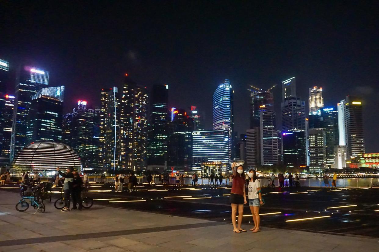 This photograph taken February 13, 2021 shows people taking photos against the city skyine in Singapore. (Photo by Roslan Rahman / AFP) (Photo by ROSLAN RAHMAN/AFP via Getty Images)