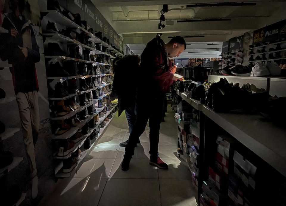 People use their mobile phone lamps to look at items at a sporting goods store during a power outage, after critical civil infrastructure was hit by a Russian missile attacks in Ukraine, as Russia's invasion of Ukraine continues, in Kyiv, November 26, 2022.  REUTERS/Gleb Garanich