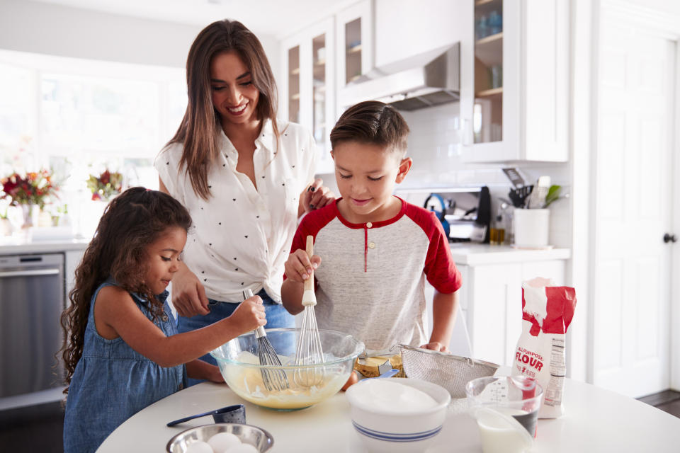 Brother and sister making cake mixture together at the kitchen table with their mum, waist up (Photo: monkeybusinessimages via Getty Images)