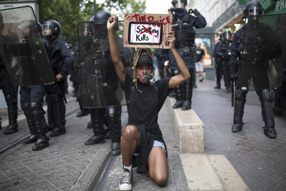 A protester kneels in front of French riot police with a sign that reads "The Police Kills" in Marseille, southern France, Saturday, June 6, 2020, to protest against the recent death of George Floyd. Floyd, a black man, died after he was restrained by police officers May 25 in Minneapolis, that has led to protests in many countries and across the U.S. Further protests are planned over the weekend in European cities, some defying restrictions imposed by authorities due to the coronavirus pandemic. (AP Photo/Daniel Cole)