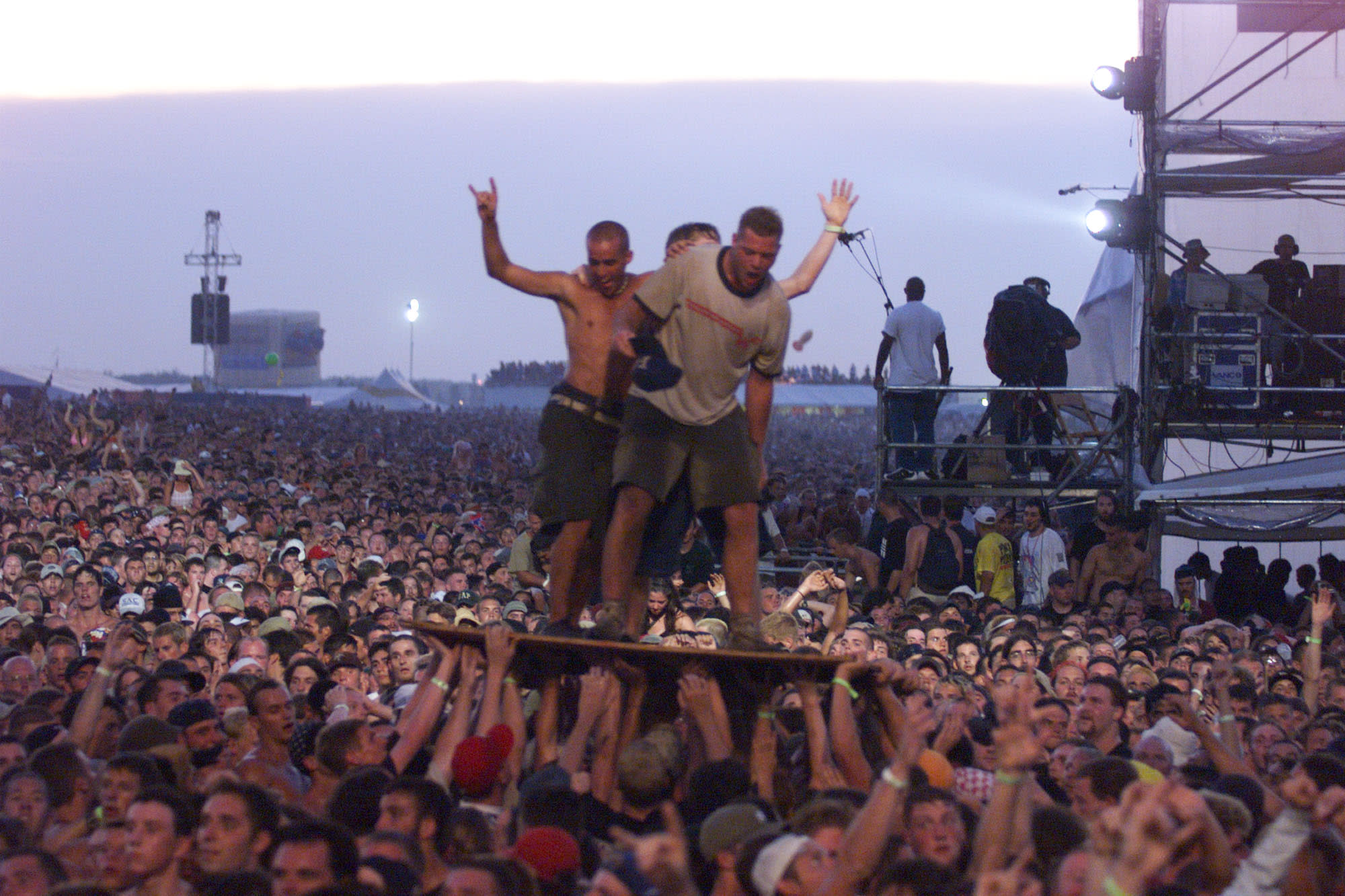 Fans stand on a stage in the middle of the crowd.