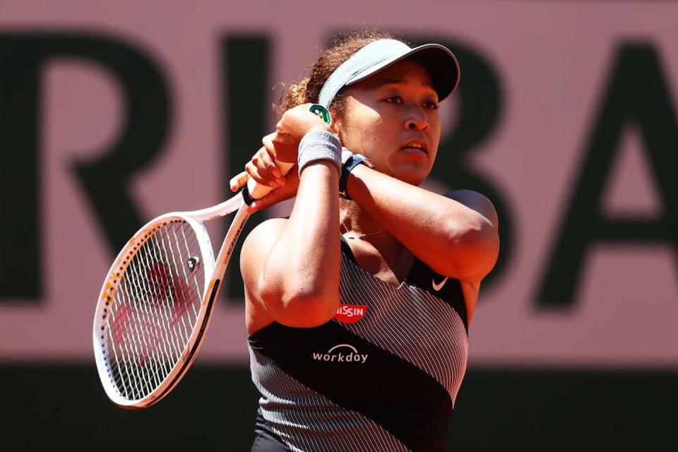 Young woman swings tennis racket.