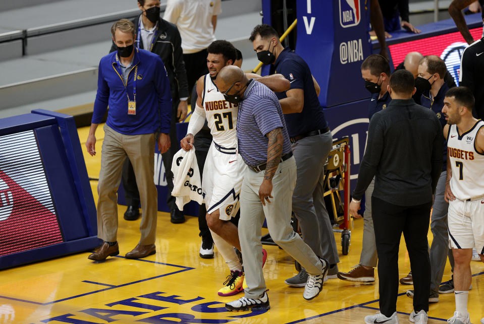 Jamal Murray #27 of the Denver Nuggets is helped off the court after an injury in their game against the Golden State Warriors at Chase Center on April 12, 2021 in San Francisco, California. NOTE TO USER: User expressly acknowledges and agrees that, by downloading and or using this photograph, User is consenting to the terms and conditions of the Getty Images License Agreement. (Photo by Ezra Shaw/Getty Images)