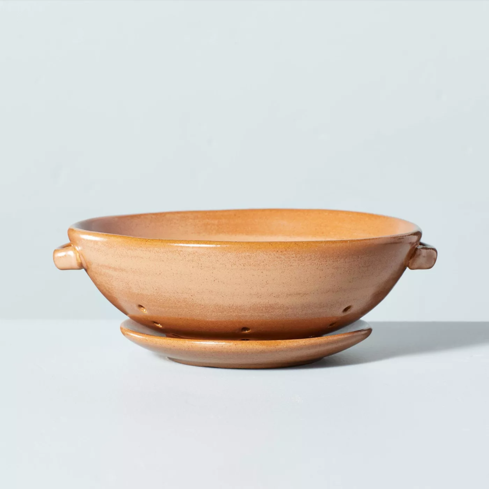 stoneware bowl with holes and matching saucer on blue backdrop