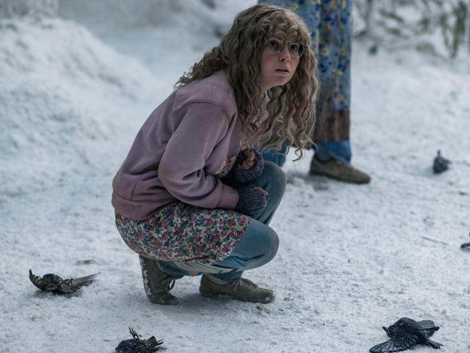 Teen Misty squats on the snowy ground in a purple sweatshirt, floral shorts, and blue tights while surrounded by dead birds.