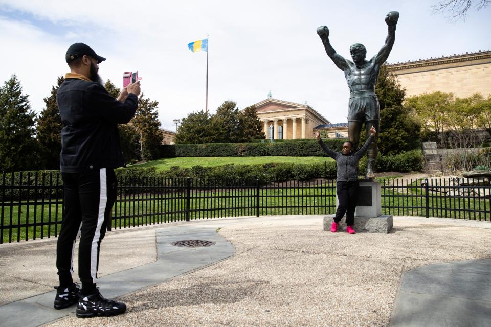 A man takes a photo of a woman in front of the Rocky Statue in Philadelphia, PA