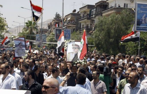 Mourners gather outside the Melkite Catholic Church of the Holy Cross as they wave the Syrian flag and hold images of assassinated Syrian Defense Minister Daoud Rajha during his funeral in Damascus