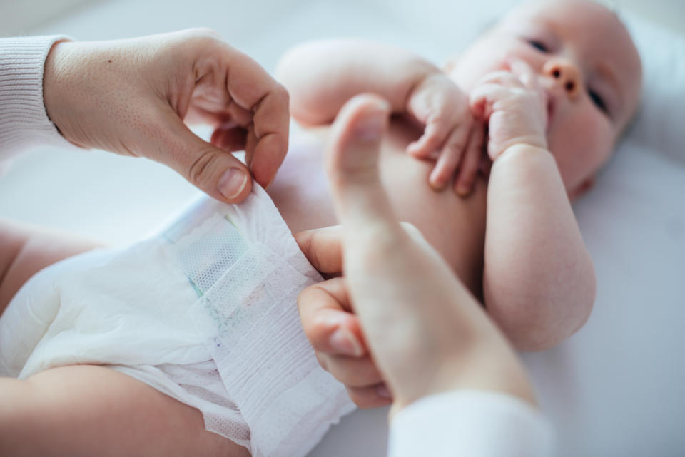 Adult hands changing a baby's diaper, baby lying down looking up