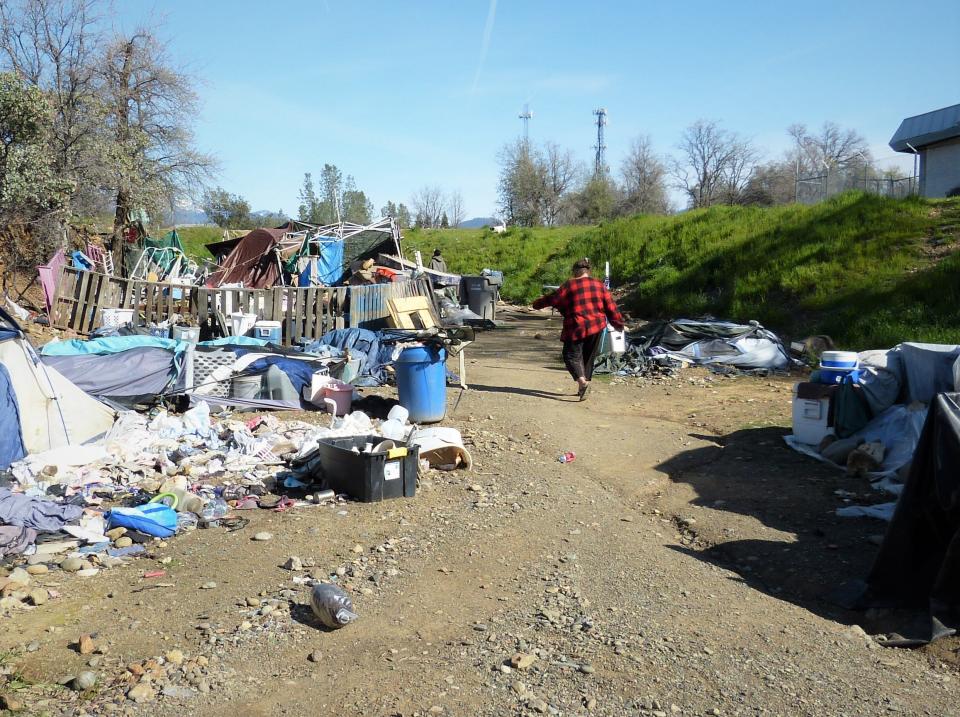 A woman walks among homeless camps near the Sulphur Creek Canyon in Redding on April 5, 2023.