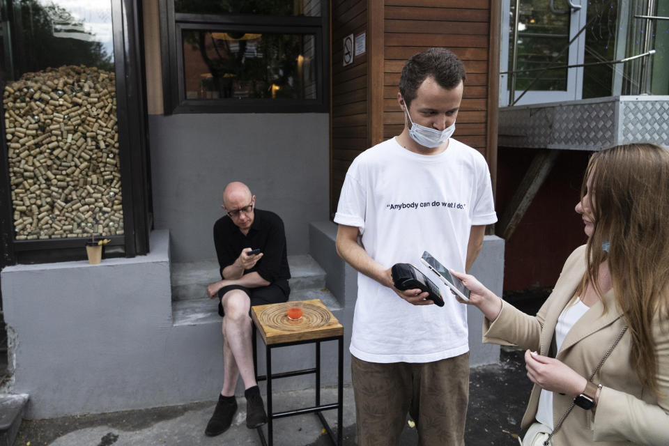 A waiter serves customers outside the Moments bar as they haven't got QR codes of vaccination or a negative coronavirus test in Moscow, Russia, Monday, June 28, 2021. Restaurants and cafes in Moscow on Monday began requesting that patrons provide proof of vaccination or a negative coronavirus test as the Russian capital faces a surge of new infections. As proof of vaccination for entering a restaurant, customers must visit a government website and get a QR code, a digital pattern designed to be read by a scanner. (AP Photo/Pavel Golovkin)