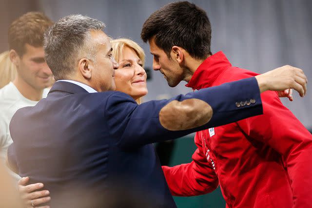 <p>Srdjan Stevanovic/Getty</p> Novak Djokovic hugs his parents, Srdjan and Dijana, after the Davis Cup World Group first round single match in Serbia on Feb. 3, 2017.