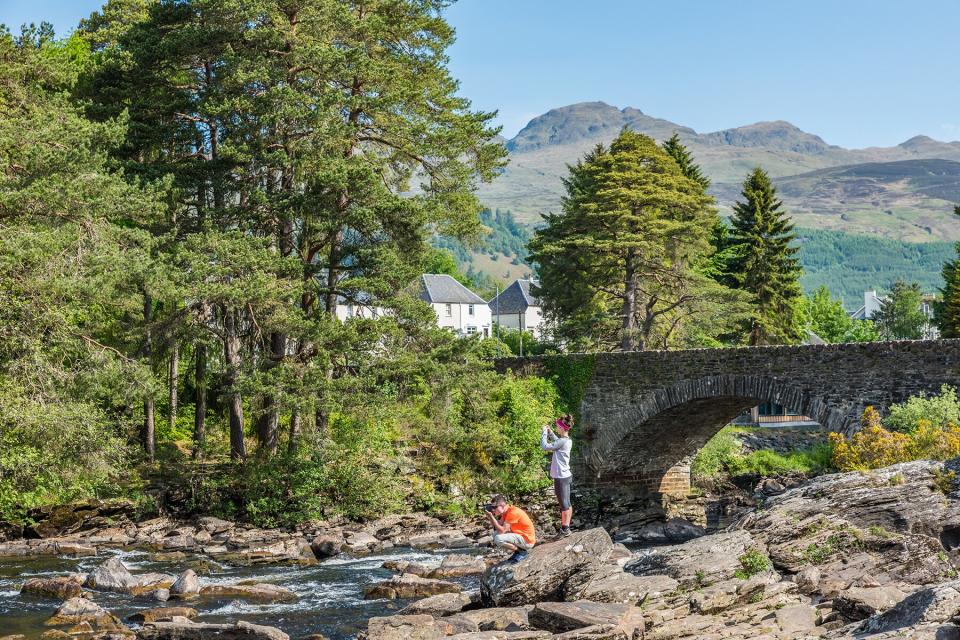 A Couple Of Tourists Taking Pictures Of Falls Of Dochart in Killin, United Kingdom