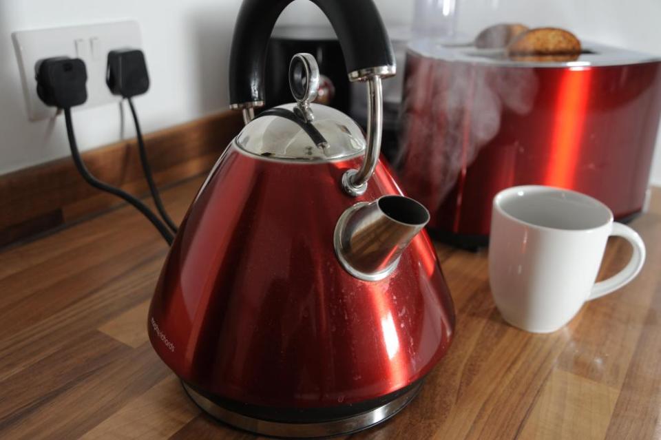 Kettle boiling with steam and toaster cooking toast behind it.