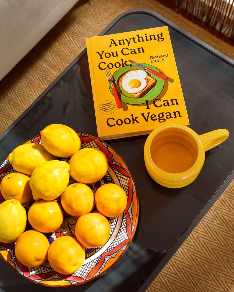 Cookbook next to orange mug and oranges.