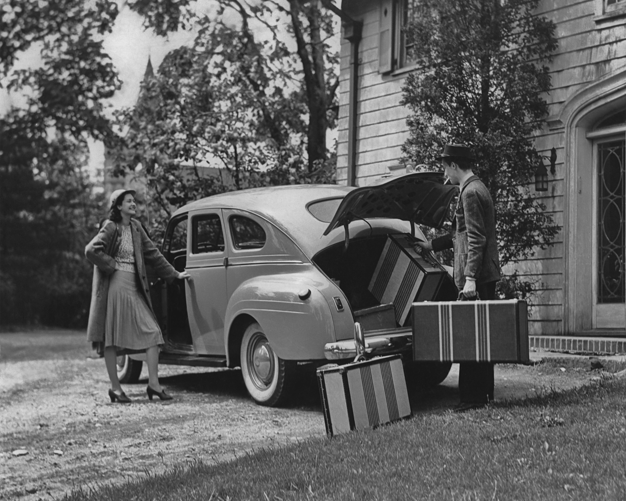 A man loads suitcases in to the boot of a car, as a woman looks on, in the 1940's.