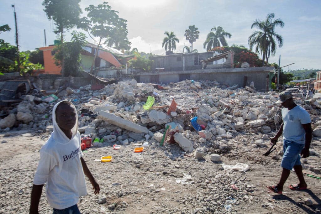 Men walk among the debris of a collapsed building after a 7.2-magnitude earthquake struck Haiti on August 16, 2021 in Corvalion, Les Cayes, Haiti. (Photo by Richard Pierrin/Getty Images)