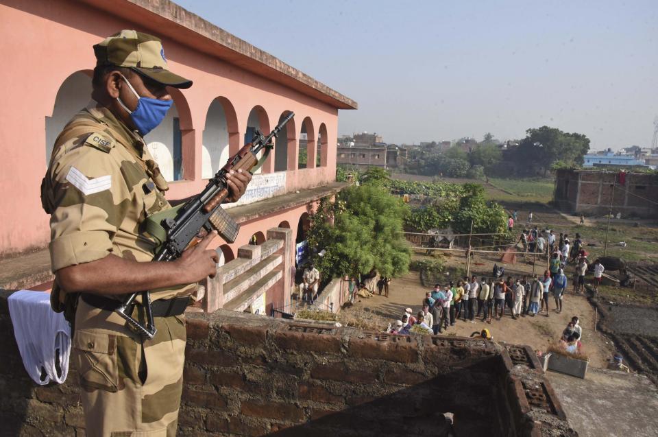 A security officer stands guard as voters stand in a queue outside a polling station at Masaudhi, in the eastern Indian state of Bihar, Wednesday, Oct. 28, 2020. Voting began Wednesday in India’s third-largest state of Bihar, the first major election in the country since the pandemic and a test for Prime Minister Narendra Modi’s popularity as he faces criticism on many fronts. (AP Photo/Aftab Alam Siddiqui)