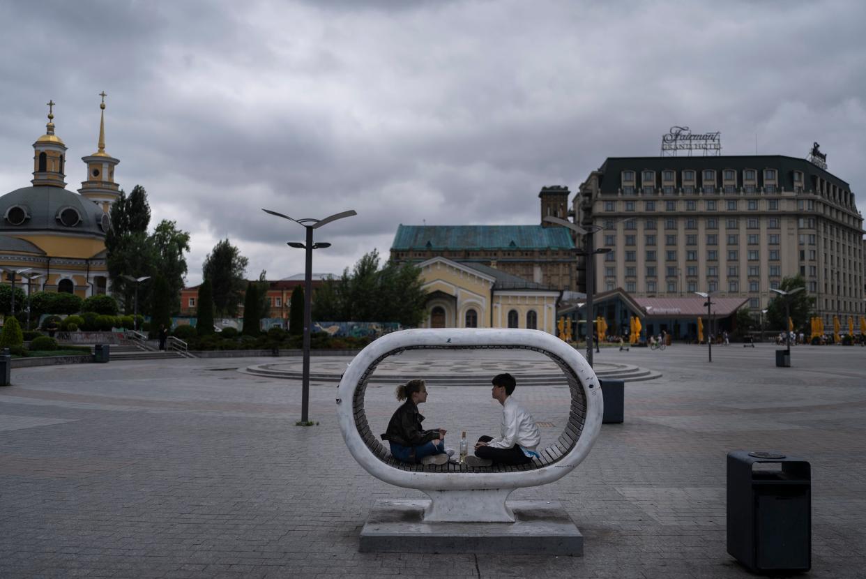 A couple with wine bottles chat on a bench in the Podil neighborhood of Kyiv (AP)