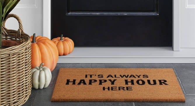 A brown doormat that reads "It's Always Happy Hour Here'