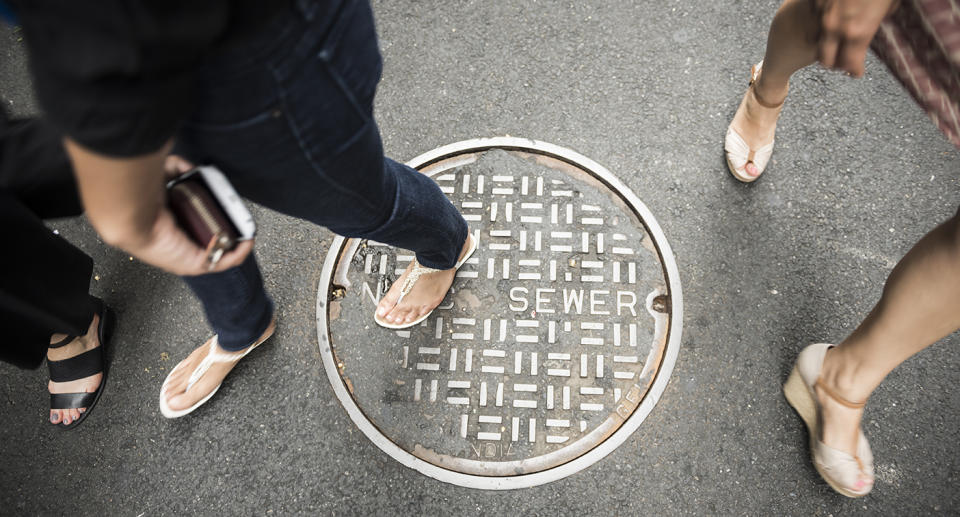 A group of women walking walk over a sewer manhole cover.