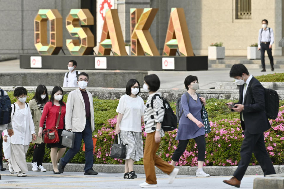 People wearing face masks walk by the city hall in Osaka, western Japan, May 14, 2021. Hospitals in Osaka, Japan’s third-biggest city and only 2 1/2 hours by bullet train from Summer Olympics host Tokyo, are overflowing with coronavirus patients. About 35,000 people nationwide - twice the number of those in hospitals - must stay at home with the disease, often becoming seriously ill and sometimes dying before they can get medical care. (Kyodo News via AP)