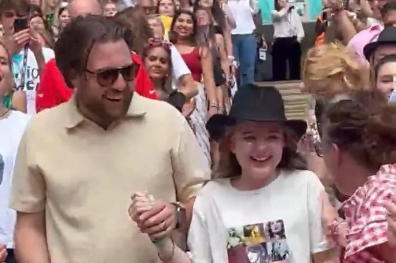 Nik Oliver and Elsie Oliver walk back down the stairs to their seats after being given the 22 hat by Taylor Swift