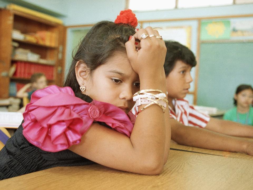 A girl rests her head in her hands in a classroom in 1993