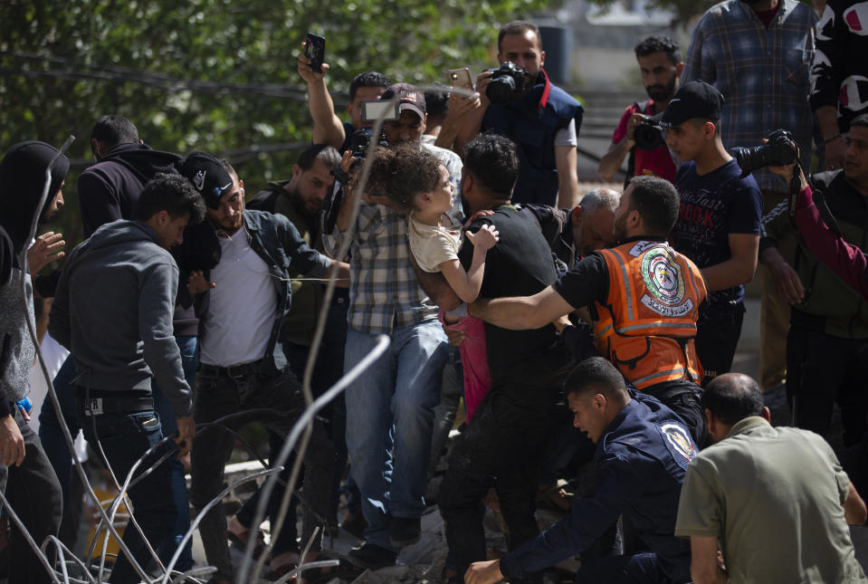 Palestinos sacan a una niña el domingo 16 de mayo de 2021 de entre los escombros de un edificio residencial destruido por un bombardeo de Israel, en Gaza. (AP Foto/Khalil Hamra)